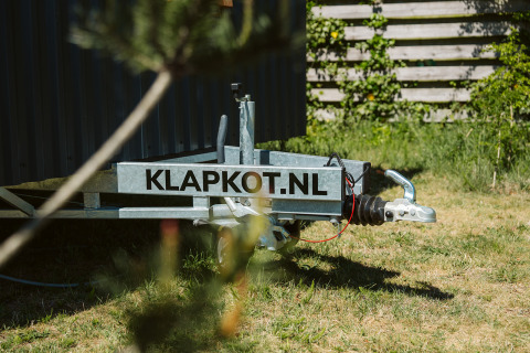 Primo piano di un rimorchio con scritta KLAPKOT.NL accanto a una tiny house a De Klepperstee, Paesi Bassi.