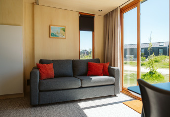 Lichte zithoek in tiny house Klapkot C20 met grijze bank en rode kussens bij De Klepperstee, Nederland.