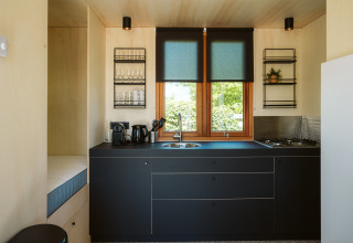 Cocina moderna de tiny house con armarios negros, ventanas grandes y decoración minimalista en Klapkot C20.