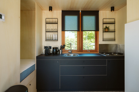 Moderne tiny house keuken met zwarte kasten, grote ramen en minimalistische stijl in Klapkot C20, De Klepperstee.