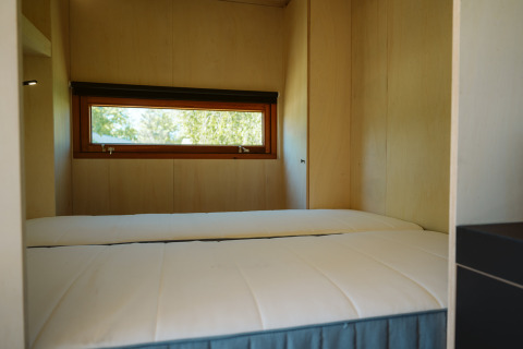 Camera da letto con due letti singoli e finestra stretta in una tiny house a De Klepperstee, Paesi Bassi.