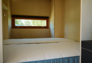Slaapkamer met twee eenpersoonsbedden en een smal raam in een tiny house op De Klepperstee, Nederland.