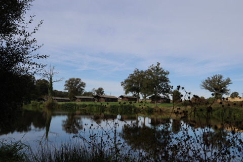 Zicht op meer en groene weiden met lodges in Domaine Bonneblond, vakantiepark in Auvergne-Rhône-Alpes, Frankrijk.