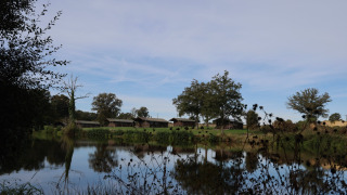 Vista de lago y campos verdes con cabañas en Domaine Bonneblond, parque vacacional en Auvergne-Rhône-Alpes, Francia.