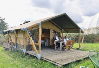 Family gathers around a table in front of a safari tent at Domaine Bonneblond holiday park in Auvergne-Rhône-Alpes, France.