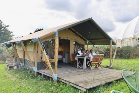 Gezin aan tafel voor een safaritent op Domaine Bonneblond vakantiepark in Auvergne-Rhône-Alpes, Frankrijk.