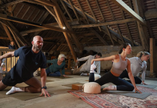 A group practices yoga in a rustic attic at Domaine Bonneblond holiday park in Auvergne-Rhône-Alpes, France.