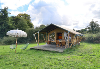 Glamping tent with wooden deck, chairs and umbrella at Domaine Bonneblond holiday park in Auvergne-Rhône-Alpes.