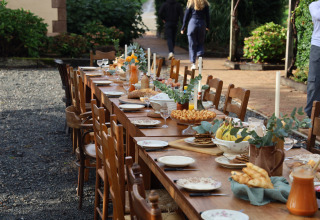 Outdoor wooden dining table at Domaine Bonneblond set for brunch with pastries, fruits, juice and plates.