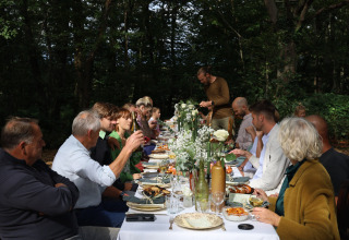 Gæster nyder en fælles middag udendørs i skoven på Domaine Bonneblond feriepark i Auvergne-Rhône-Alpes.