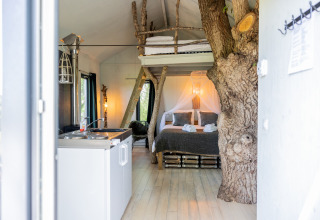 Gemütliches Baumhaus-Interieur mit Baumstamm, Küchenzeile und Bett im Domaine Bonneblond, Auvergne, Frankreich.