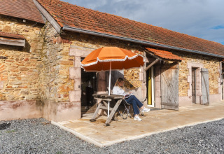 Vrouw ontspant onder een oranje parasol voor een stenen huisje bij Domaine Bonneblond, Auvergne-Rhône-Alpes, Frankrijk.