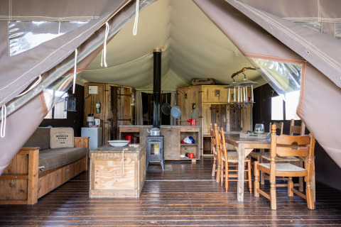 Binnenaanzicht van een tent met houten meubels en eettafel bij Domaine Bonneblond in Auvergne-Rhône-Alpes, Frankrijk.