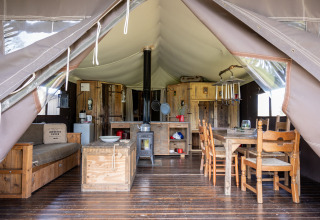 Vue intérieure d'une tente avec mobilier en bois et table à manger au Domaine Bonneblond en Auvergne-Rhône-Alpes, France.