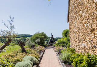 Gepflasterter Weg mit Blumen und Bäumen neben einem Steingebäude in Domaine Bonneblond, Auvergne-Rhône-Alpes, Frankreich.