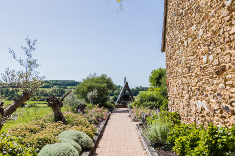 Gepflasterter Weg mit Blumen und Bäumen neben einem Steingebäude in Domaine Bonneblond, Auvergne-Rhône-Alpes, Frankreich.