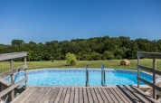 Udsigt over en swimmingpool med træterrasse og grønne marker på Domaine Bonneblond i Auvergne-Rhône-Alpes.