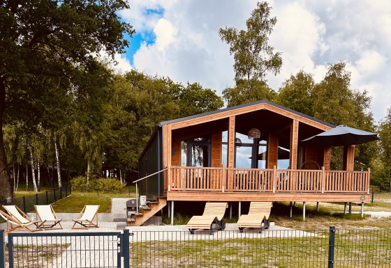 Modern Lakehouse Scandi bij Wilsumer Berge, Duitsland, met houten terras en ligstoelen in groene omgeving.
