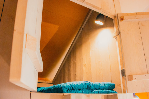 Acogedor rincón para dormir con paredes de madera y ropa de cama azul en Safari cottage en De Boshoek.