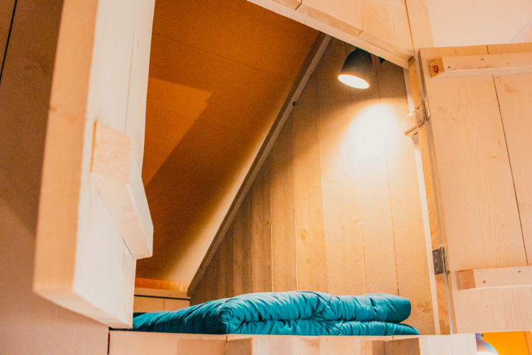 Gemütliche Bettnische mit Holzverkleidung und blauem Bettzeug im Safari Cottage im Ferienpark De Boshoek.