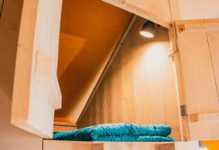 Cozy sleeping nook with wood paneling and blue bedding in the Safari cottage at De Boshoek in the Netherlands.