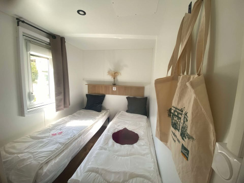 Et lyst værelse med to enkeltsenge, vindue og indkøbsposer i Cottage ved Domaine Seasonova Saâne et Mer.