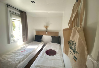 Et lyst værelse med to enkeltsenge, vindue og indkøbsposer i Cottage ved Domaine Seasonova Saâne et Mer.