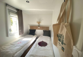 Et lyst værelse med to enkeltsenge, vindue og indkøbsposer i Cottage ved Domaine Seasonova Saâne et Mer.