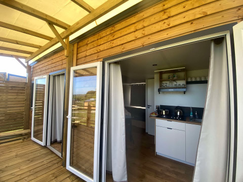Terraza de madera y puertas de vidrio abiertas hacia una cocina moderna en una cabaña en Domaine Seasonova Saâne et Mer, Francia