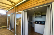 Terraza de madera y puertas de vidrio abiertas hacia una cocina moderna en una cabaña en Domaine Seasonova Saâne et Mer, Francia