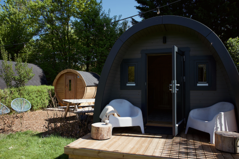 Glamping pod med sauna, terrasse med hvide stole og grøn have, perfekt til afslappende udendørs ophold.