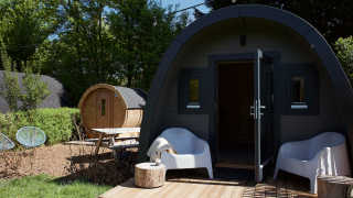 Glamping pod met sauna, terras met witte stoelen en een groene omgeving, ideaal voor ontspanning.