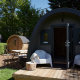 Glamping pod med sauna, terrasse med hvide stole og grøn have, perfekt til afslappende udendørs ophold.
