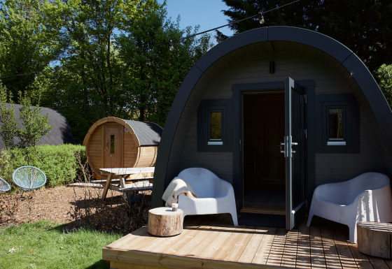 Glamping pod with sauna, deck with white chairs, and lush greenery, perfect for a relaxing outdoor retreat.