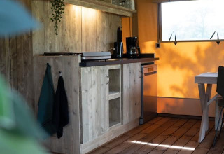 Rincón de cocina rústica en una tienda safari con paredes de madera, estantería abierta y luz natural.