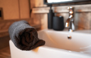 Asciugamano grigio arrotolato sul bordo di una vasca da bagno in una tenda safari con rubinetto moderno.