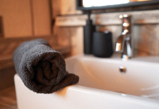 Asciugamano grigio arrotolato sul bordo di una vasca da bagno in una tenda safari con rubinetto moderno.