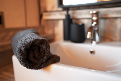 Serviette grise roulée sur la baignoire d'une tente safari avec robinet moderne en arrière-plan.