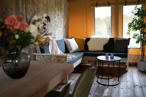 Gemütlicher Wohnbereich in einem Safarizelt mit Holzmöbeln, Sofaecke, Pflanzen und Dekoration.