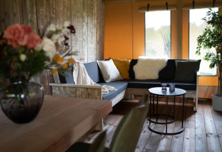 Cozy interior of a safari tent with wooden furniture, flowers, sofa with cushions, and a small table.