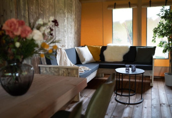 Gemütlicher Wohnbereich in einem Safarizelt mit Holzmöbeln, Sofaecke, Pflanzen und Dekoration.