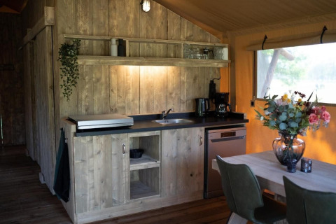 Gemütliche Küche im Safarizelt mit Holzmöbeln, Esstisch, Blumen und großem Fenster zur Natur.