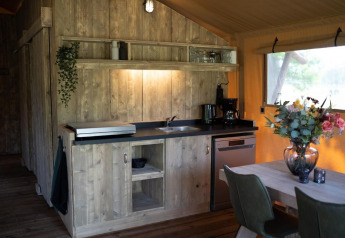 Accogliente cucina in tenda safari con arredi in legno, tavolo da pranzo con fiori e vista sulla natura.