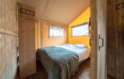 Interno di una comoda camera in una tenda safari, con letto matrimoniale e pavimento in legno.