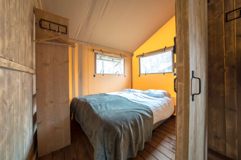 Gezellige slaapkamer in een safaritent met houten vloer, tweepersoonsbed en warme lichtinval.