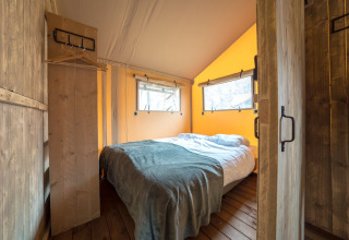 Sfeervolle slaapkamer in een safaritent met houten vloer en tweepersoonsbed, veel natuurlijk licht.