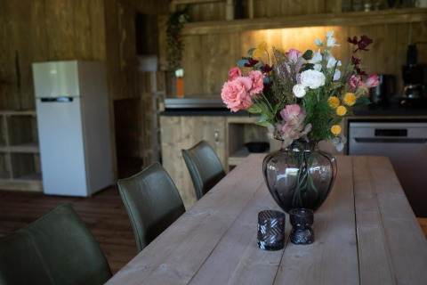 Bloemenboeket in glazen vaas op houten tafel in safari tent keuken met zicht op de koelkast.