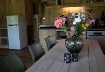 Blumenstrauß in einer Glasvase auf einem Holztisch in einer Safarizeltküche mit Kühlschrank.