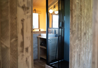 Vista de un baño moderno con paredes de madera y ducha de cristal en el interior de una tienda safari.