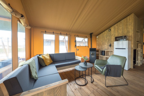 Cozy safari tent interior with wooden flooring, modern seating, large windows, and a kitchen area.
